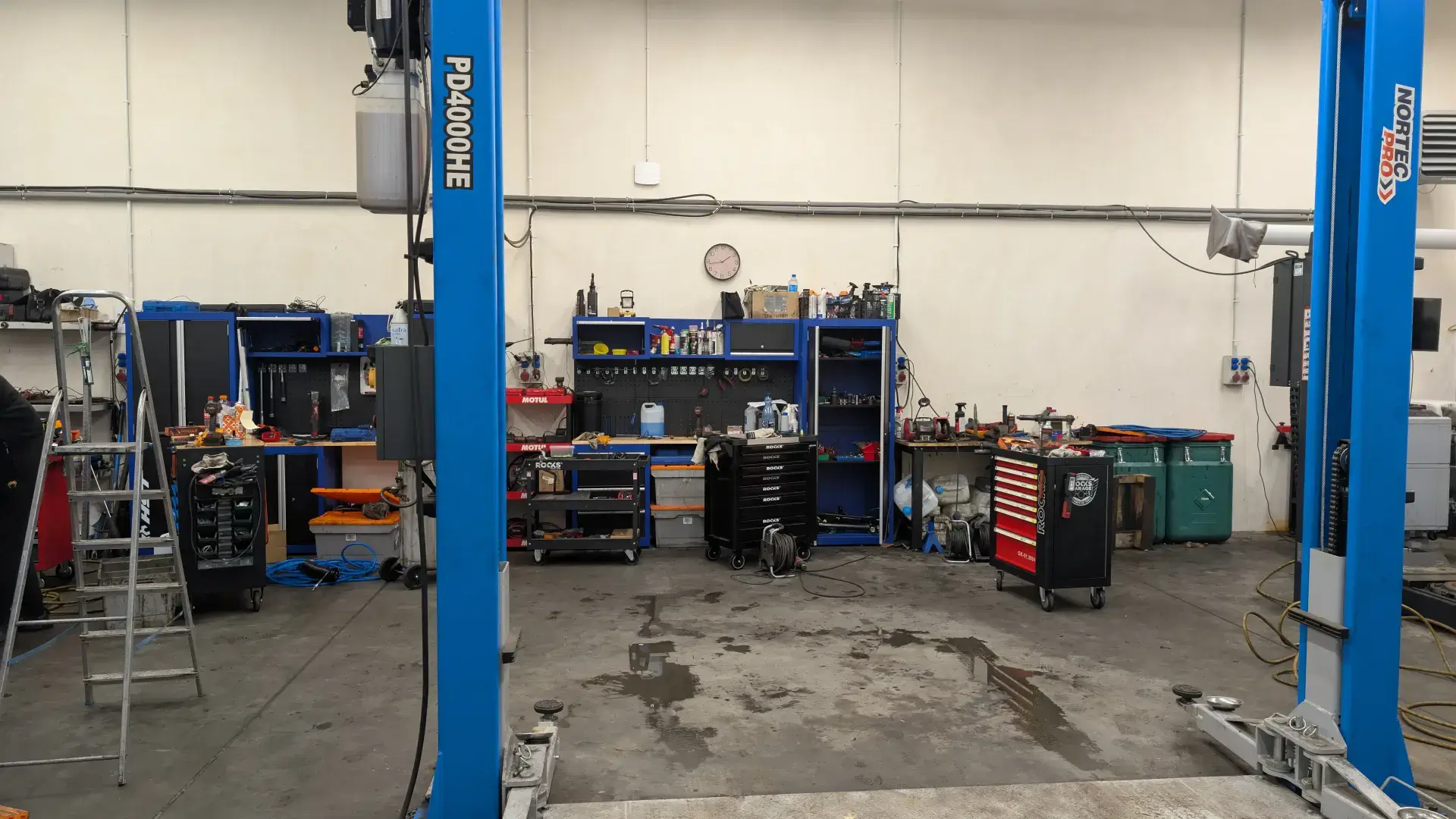 Wyposażenie wnętrza warsztatu samochodowego: niebieskie podnośniki kolumnowe i wózki narzędziowe.