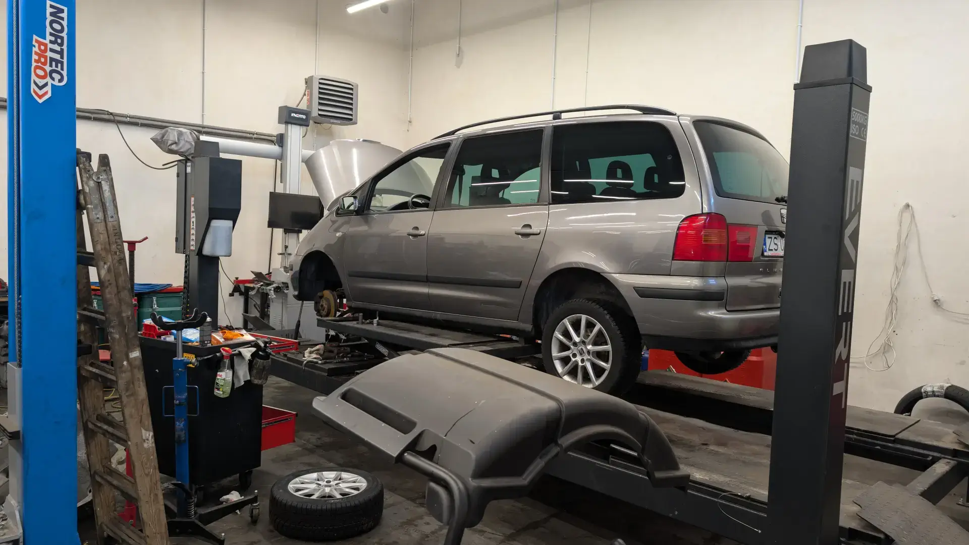 Szary Seat Alhambra na podnośniku w trakcie naprawy zawieszenia i układu jezdnego.