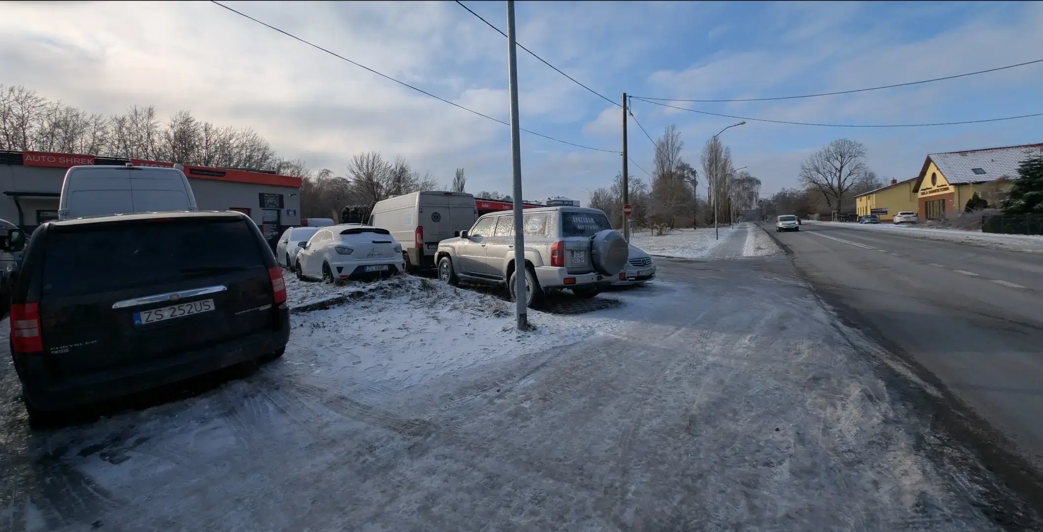Plac manewrowy warsztatu z zaparkowanymi samochodami amerykańskimi, w tym czarny Chrysler Grand Voyager.
