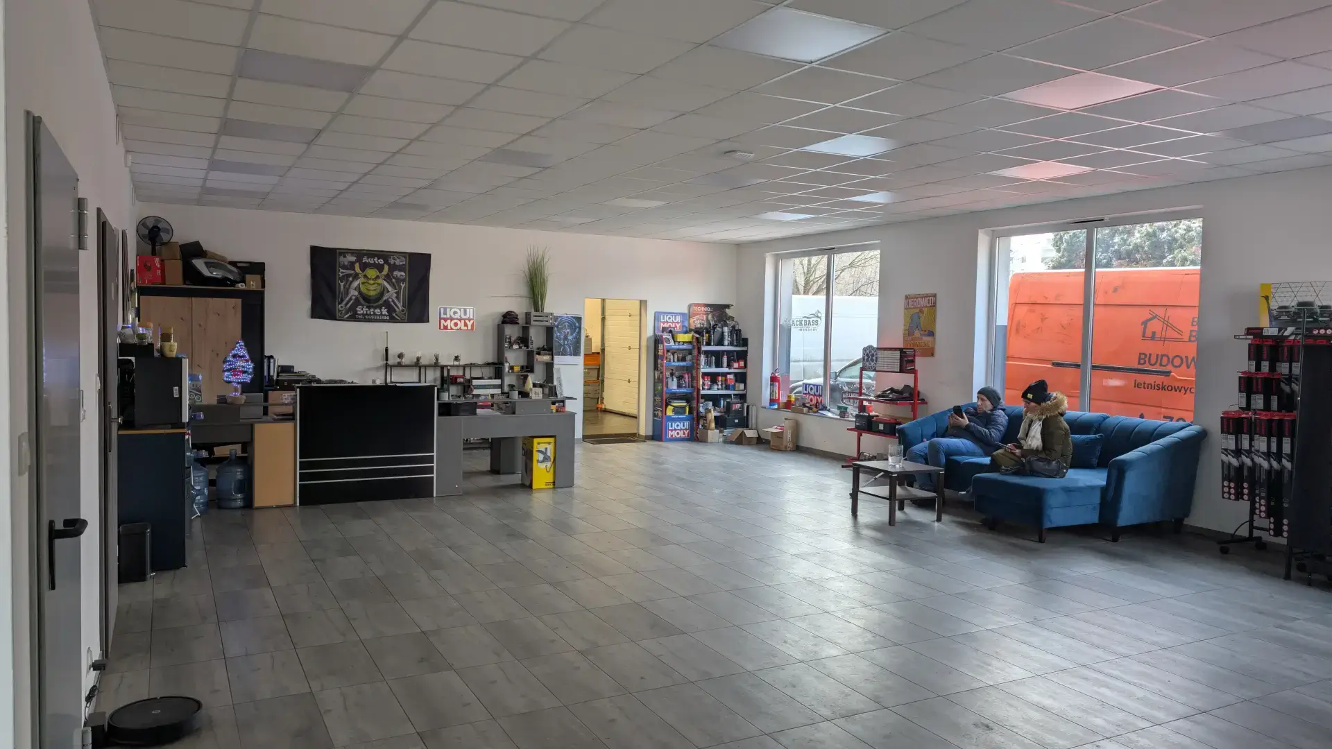 Przestronna poczekalnia dla klientów warsztatu z wygodną kanapą i stoiskiem z akcesoriami samochodowymi.