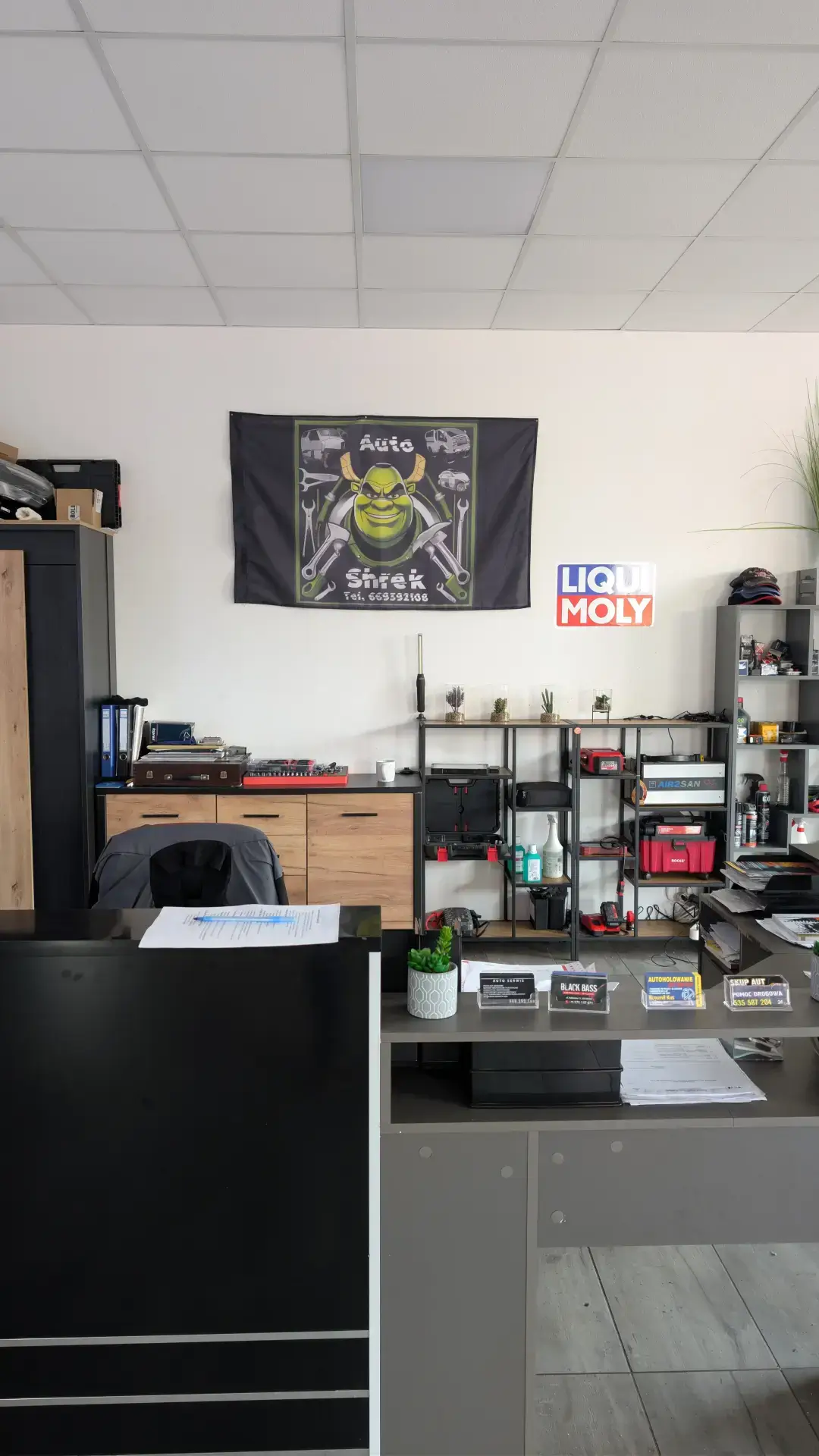 Recepcja warsztatu Autoshrek z wizytówkami usług: pomoc drogowa, skup aut i serwis mechaniczny.